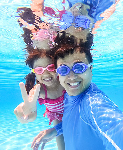 Dad and daughter take selfie smiling under water in swimming pool